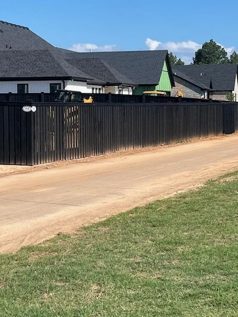 Black-stained wood privacy fence running alongside a residential driveway